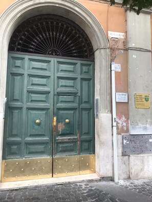 A large, green double door with a decorative metal grille above it, set in a stone archway. - Locanda San Cosimato (Rome)