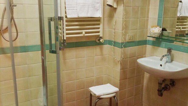 A bathroom with a glass-enclosed shower, a sink, a small stool, and a mirror. - Locanda San Cosimato (Rome)