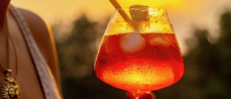 Una persona sosteniendo un vaso con pajita, con un atardecer de fondo.