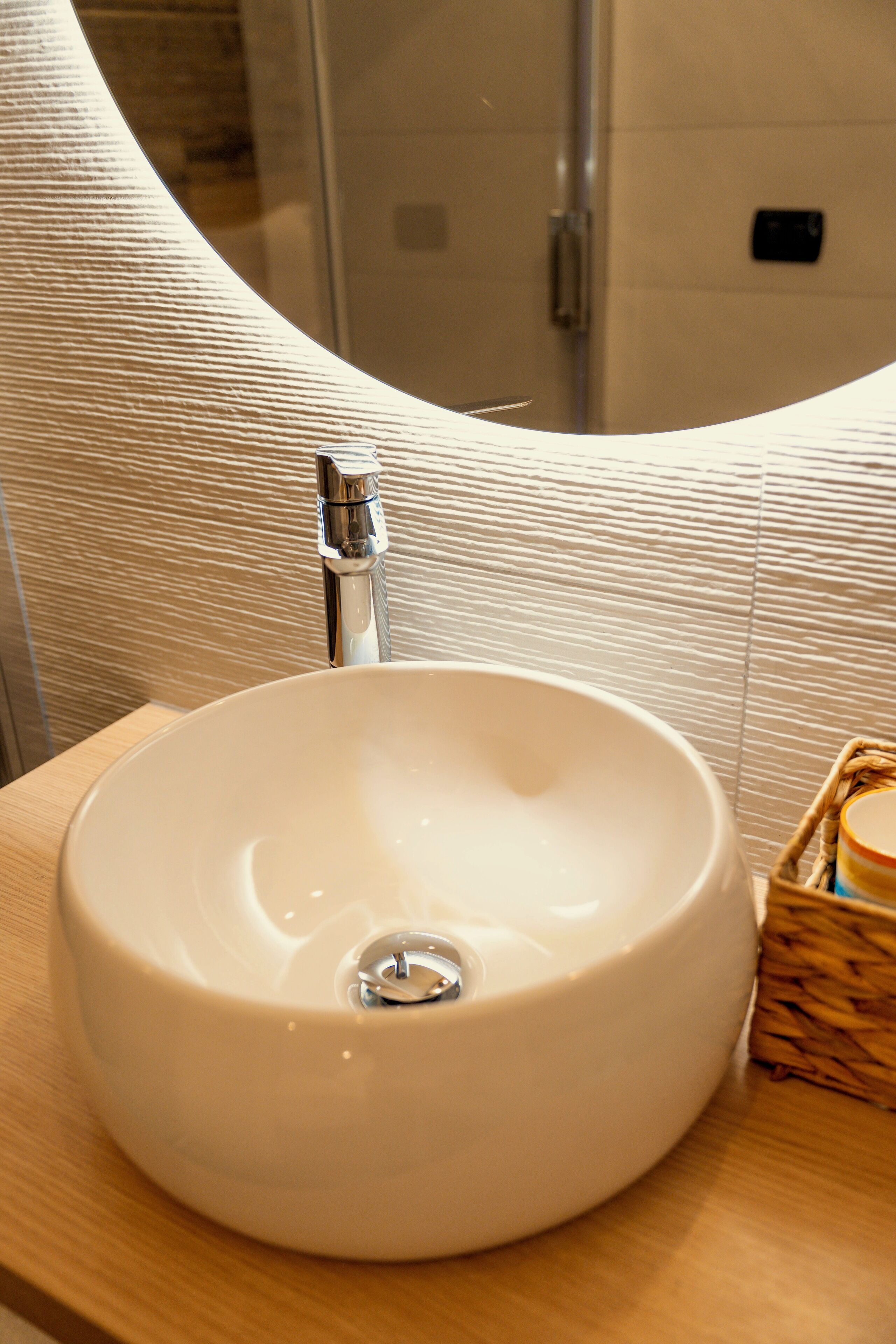 A bathroom with a round white sink, a chrome faucet, and a wooden vanity.