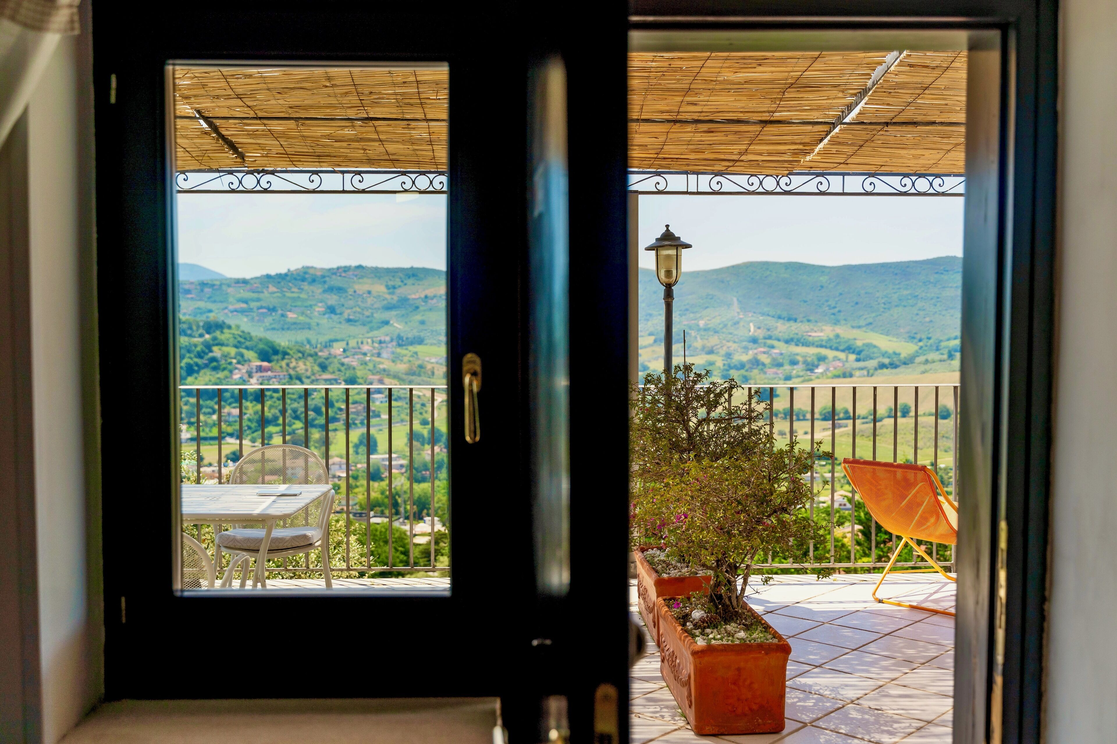 A balcony with a view of a hilly landscape, a table and chairs, and a potted plant.