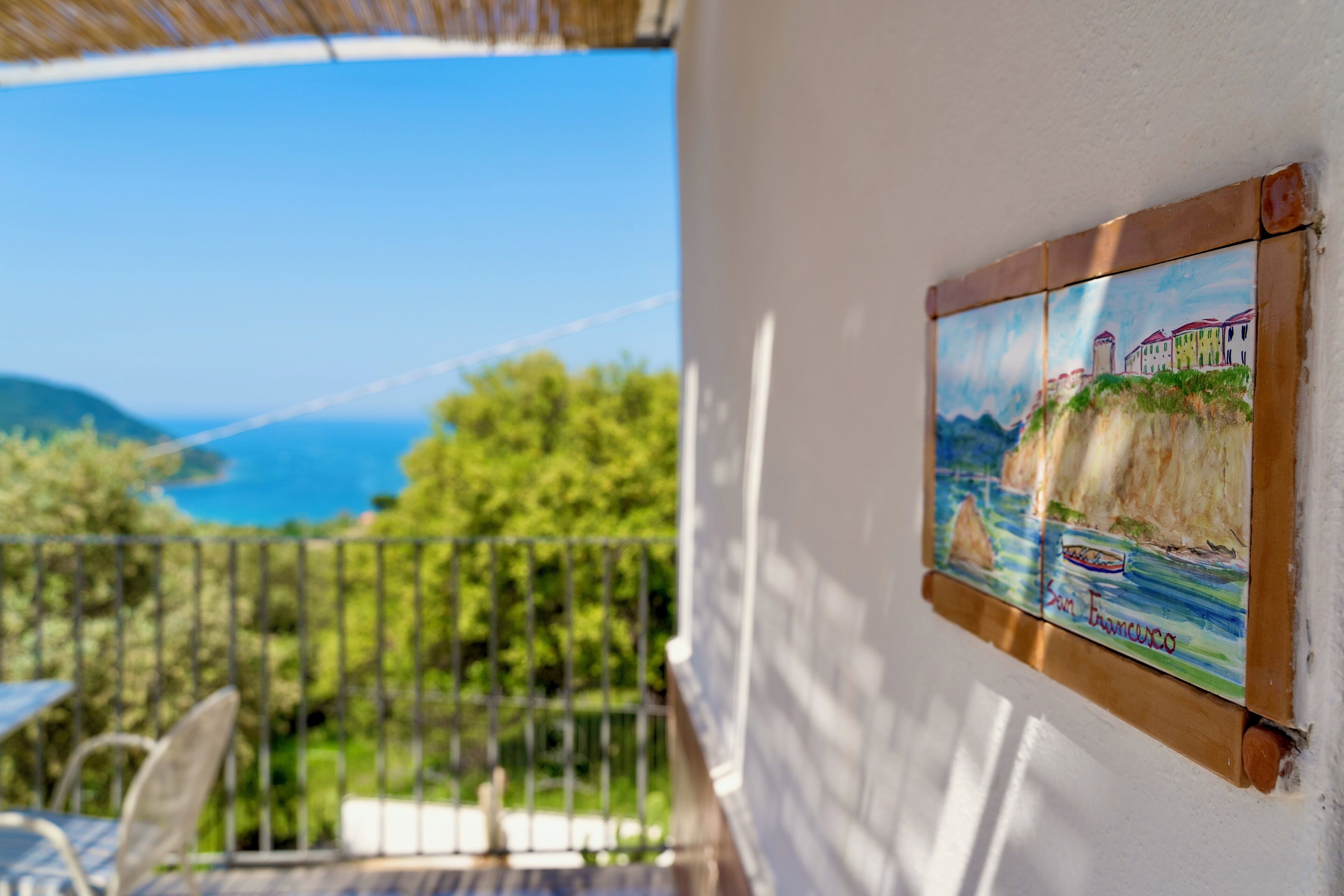 Un balcón con vista al mar y un cuadro de una escena costera.