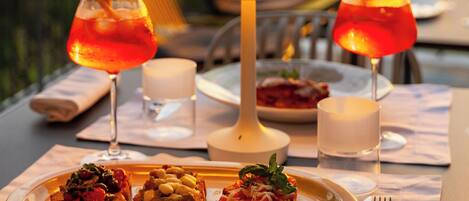 Una mesa servida con bruschetta, dos bebidas, una vela y una lámpara.