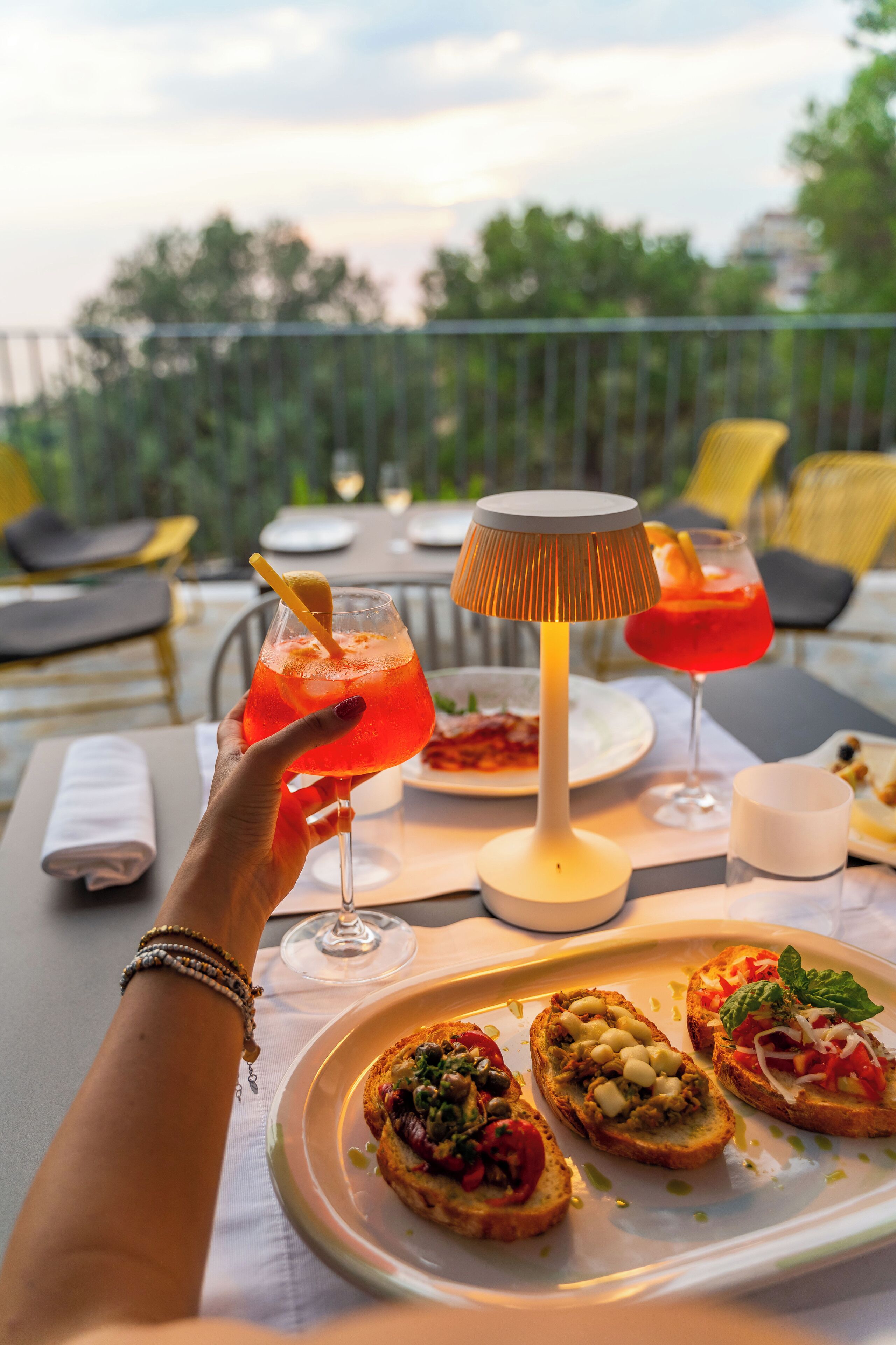 A dining table with a lamp, a plate of bruschetta, and two drinks.