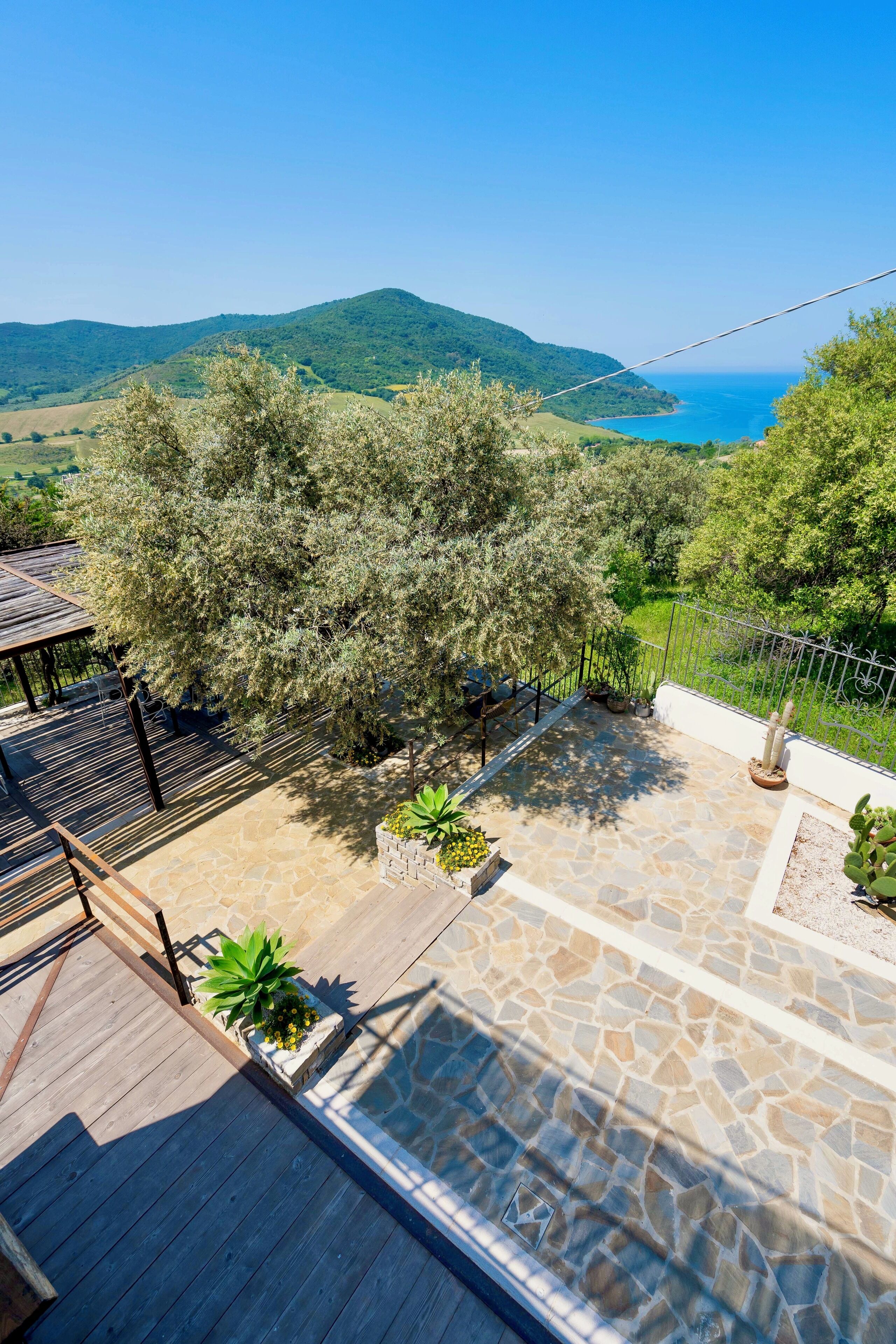 A patio area with stone flooring, a wooden deck, and a view of a coastal landscape with mountains.