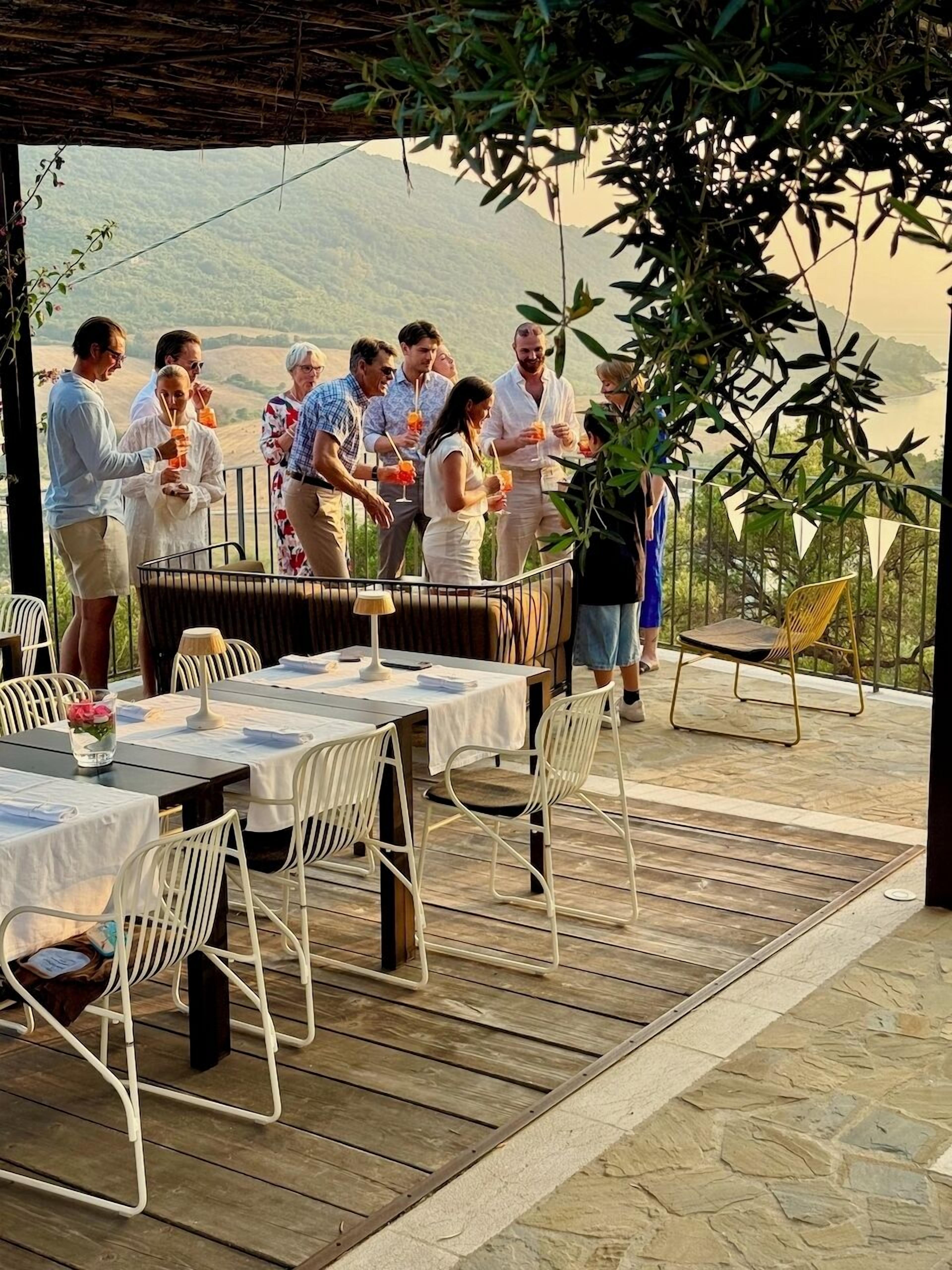 An outdoor dining area with tables and chairs, surrounded by a wooden deck and overlooking a scenic landscape.