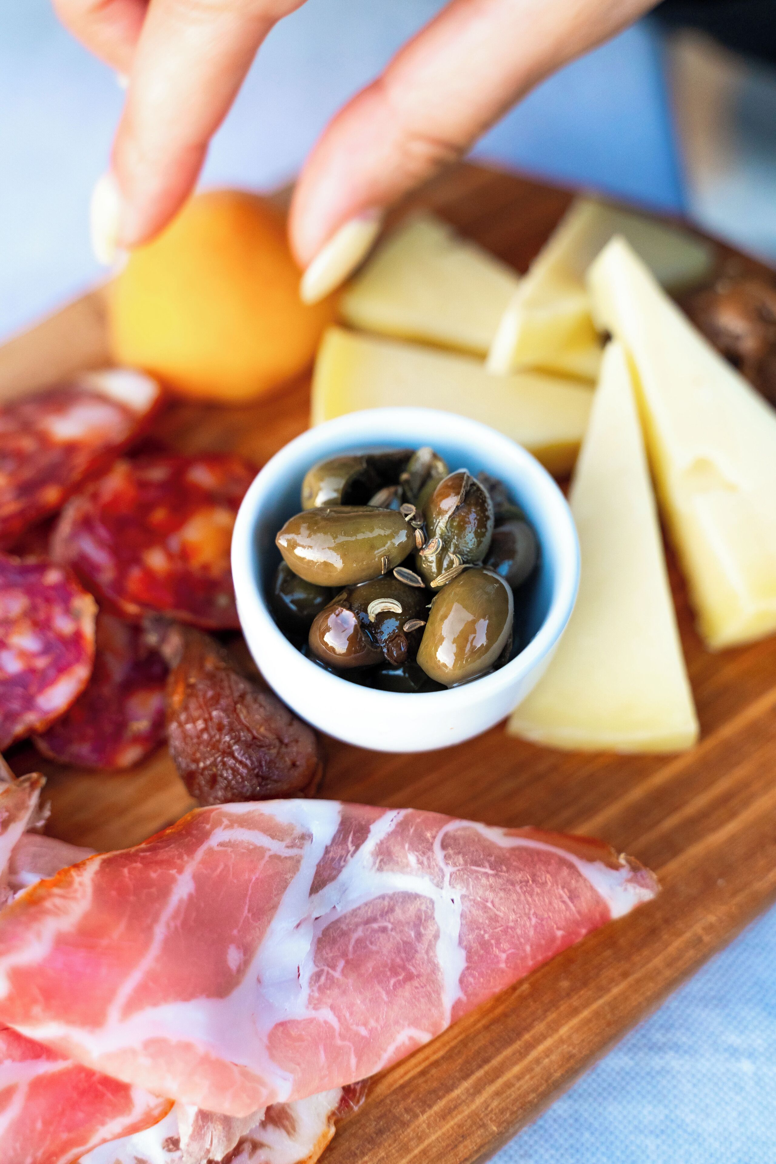 A wooden board with various cured meats, cheese, olives, and a small bowl of olives.