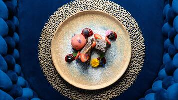 A dessert plate with various fruits and a dusting of powdered sugar, surrounded by a decorative blue and beige patterned tablecloth.
