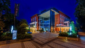 A modern hotel with a glass facade, outdoor seating, and a well-lit entrance.