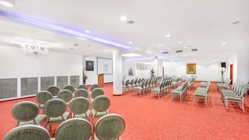 Een congreszaal met rijen stoelen, een kroonluchter en een vloer met rode vloerbedekking.