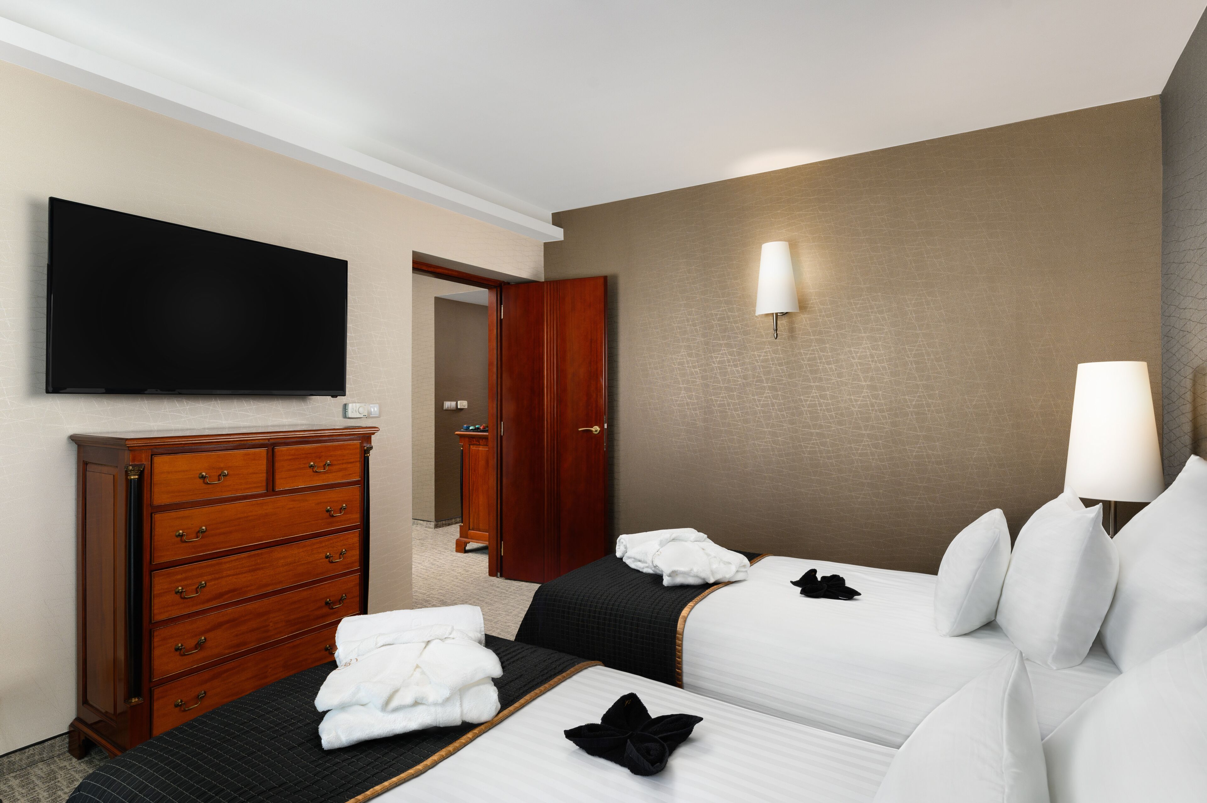 Habitación de hotel con dos camas, un televisor, un aparador de madera y una puerta que da a un baño.