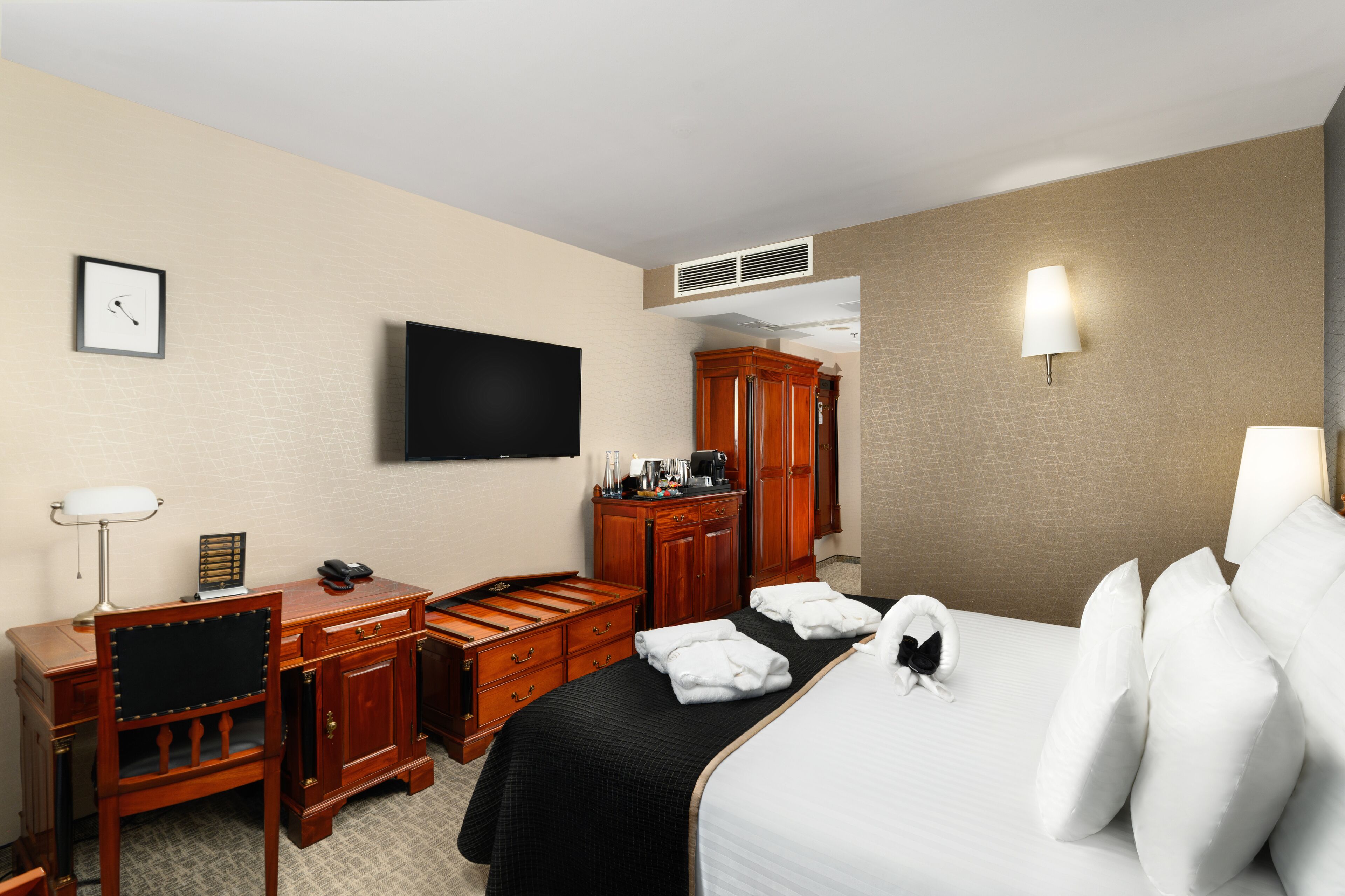 A hotel room with a bed, a desk, a chair, a television, a wardrobe, and a wall-mounted light.