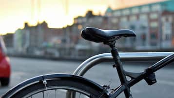Una bicicleta con asiento negro y estructura metálica, estacionada junto a un soporte para bicicletas de metal.