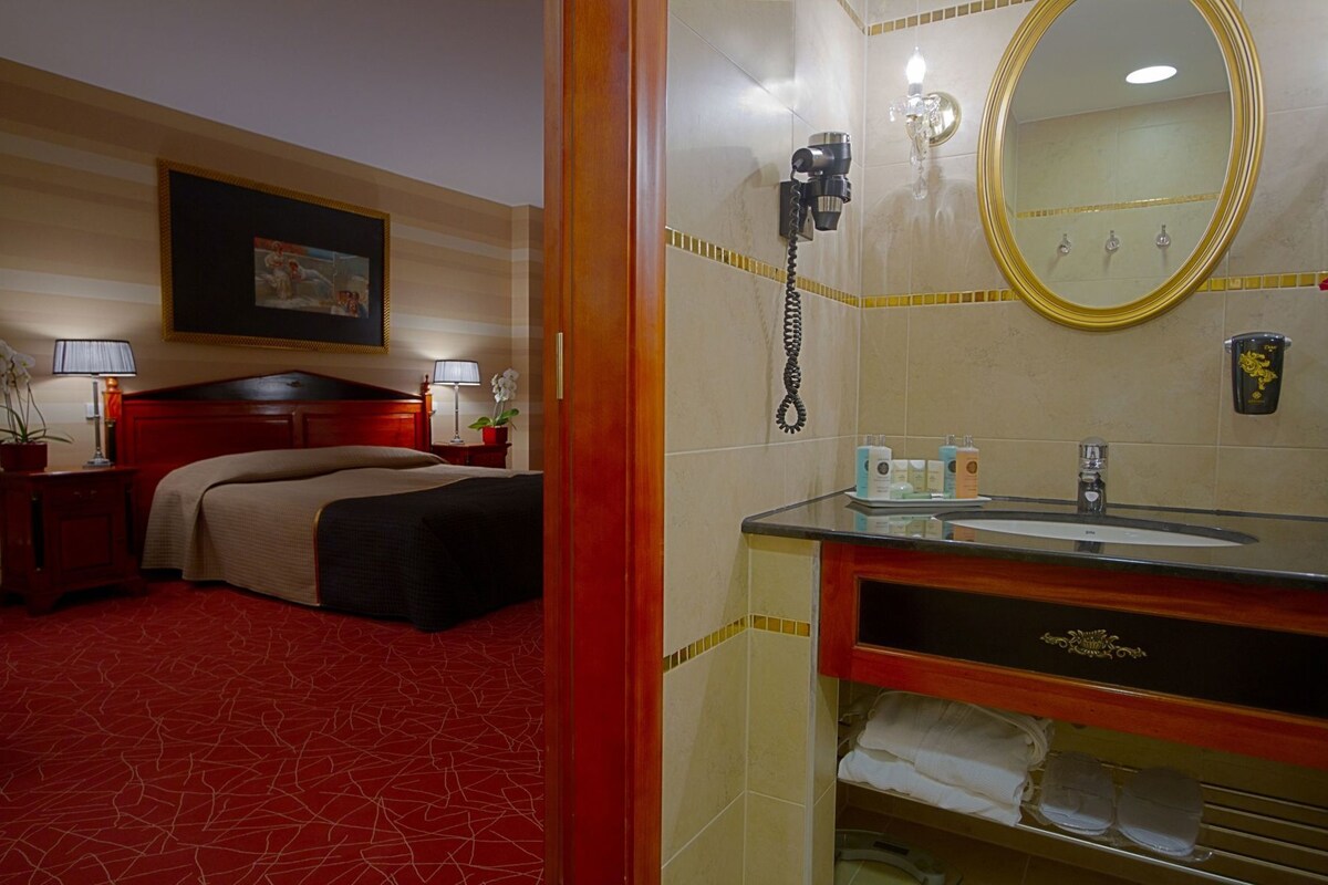Une chambre d’hôtel comprenant un lit, des lampes de chevet, un miroir, une coiffeuse avec un lavabo et des articles de toilette.