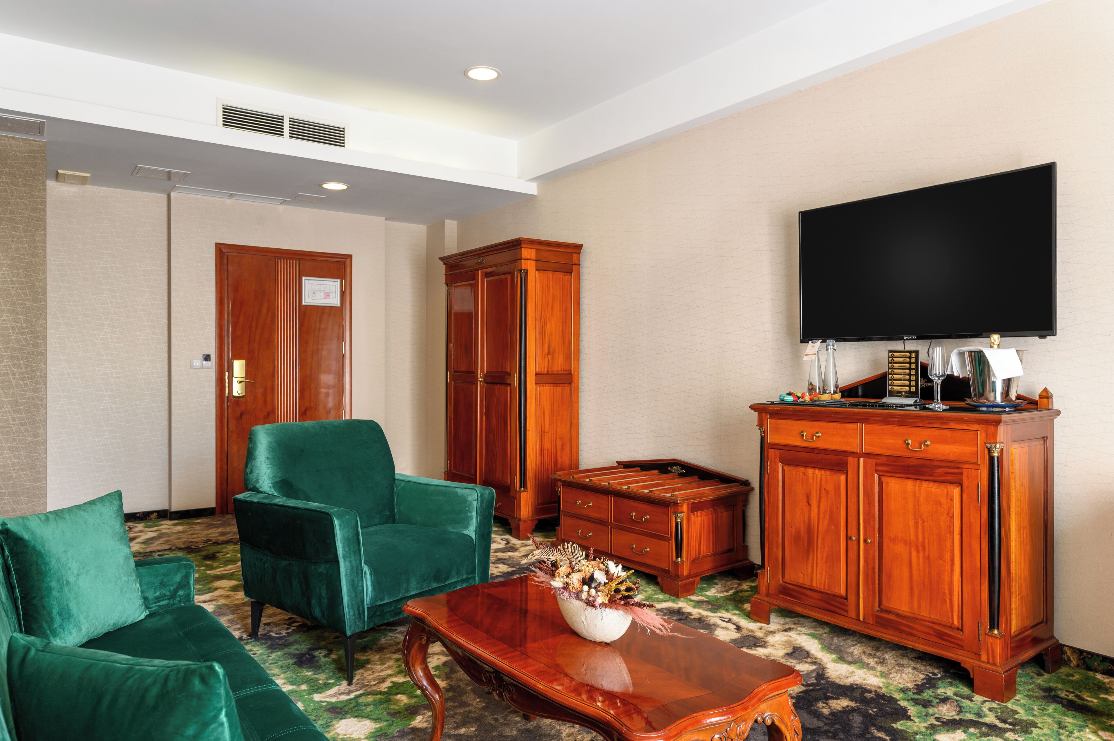 Habitación de hotel con sofá verde, un mueble de madera, un televisor de pantalla plana y una mesita de centro.
