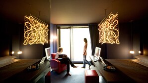 A hotel room with two beds, a red chair, and a large window. - Clocchiatti (Udine)