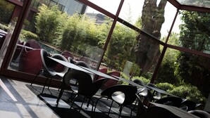 A restaurant with outdoor seating, a glass wall, and a view of greenery and a rock formation. - Clocchiatti (Udine)