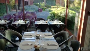 A restaurant with tables set for dining, large windows, and a view of the garden. - Clocchiatti (Udine)
