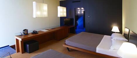 A hotel room with two beds, a desk, a television, and a seating area.