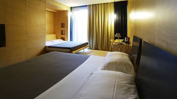 A hotel room with two beds, a desk, a chair, a lamp, and a window with curtains.