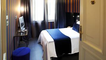 Een hotelkamer met een bed, een bureau met een computer, een stoel en een raam met gordijnen.