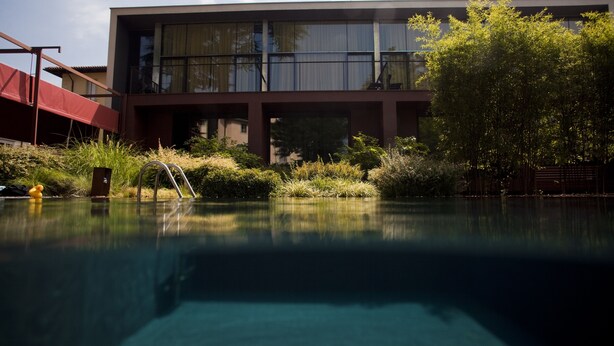 A modern building with a swimming pool, surrounded by greenery and a red structure. - Clocchiatti (Udine)