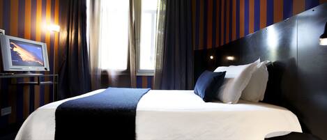 A hotel room with a bed, a TV on a stand, and curtains.