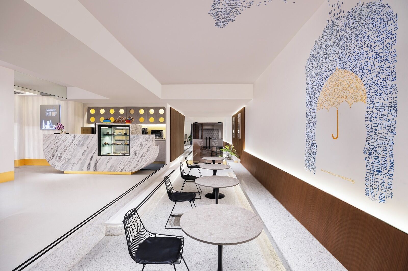 A modern hotel lobby with a marble reception desk, seating area with round tables and chairs, and a decorative wall mural.