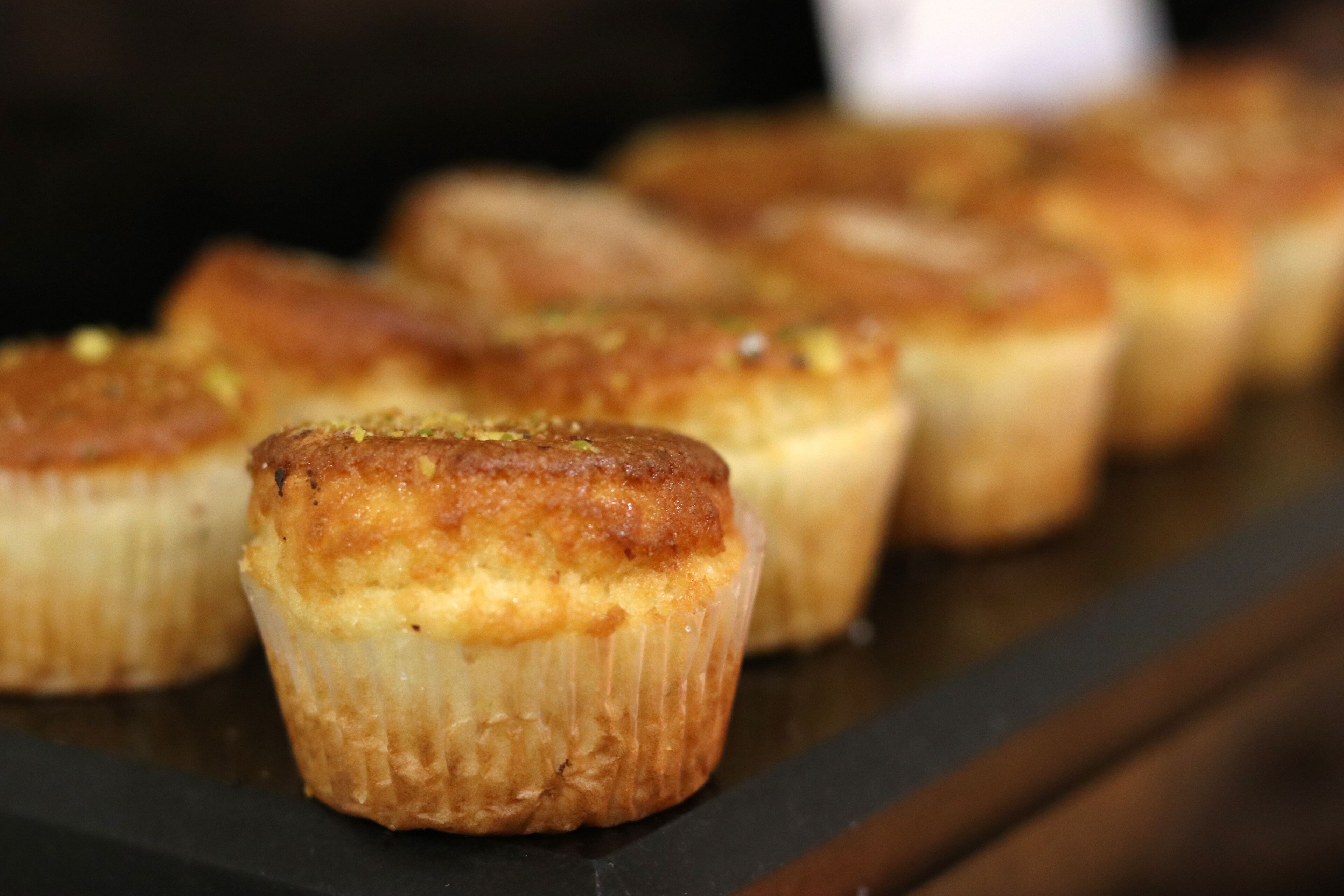 A tray of baked goods with a golden-brown crust, likely muffins or cupcakes, on a dark surface.