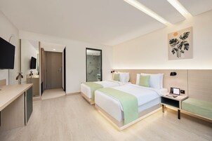 A modern hotel room with two beds, a desk, a TV, and a shower area.