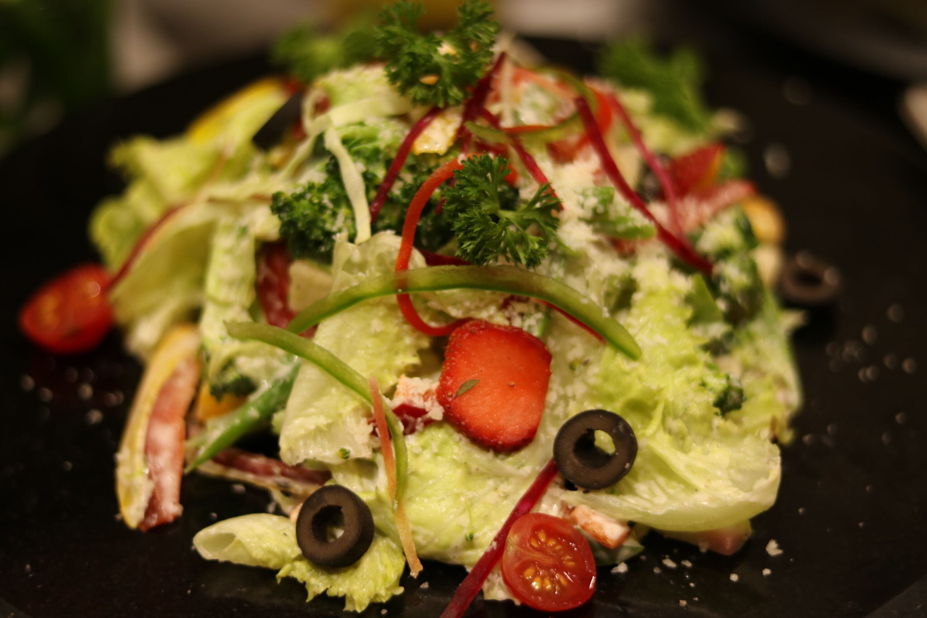 A close-up of a salad with lettuce, tomatoes, and black olives.