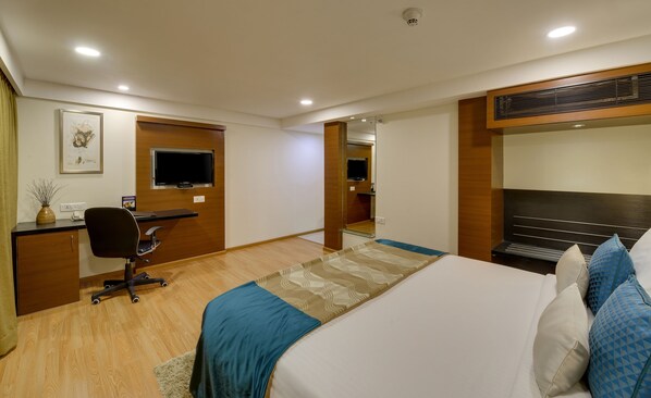 A hotel room with a bed, desk, chair, television, and a mirror.