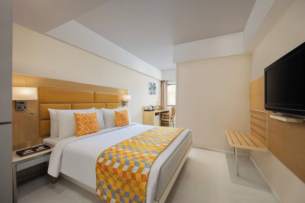 Une chambre d’hôtel comprenant un lit, une table de chevet, une lampe, une télévision et un bureau avec une chaise.