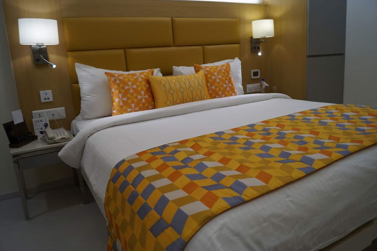 Une chambre d’hôtel avec un lit, une table de chevet avec un téléphone et deux lampes fixées au mur.