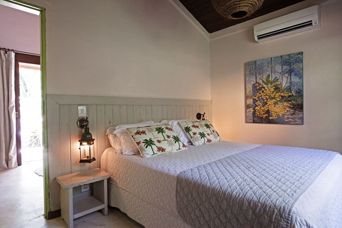 A bedroom with a bed, a nightstand, a wall-mounted air conditioner, and a painting.