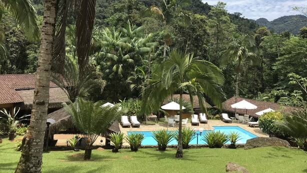 Un complexe hôtelier doté d’une piscine, de chaises longues et de cabanes à toit de chaume.