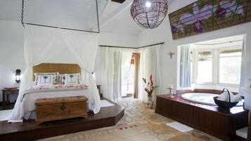 Een slaapkamer met een bed, een stenen vloer, een houten bankje, een badkuip en een hanglamp.