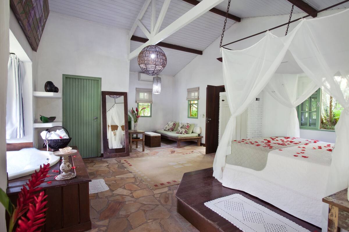A bedroom with a canopy bed, a stone floor, a green door, and a hanging light fixture.