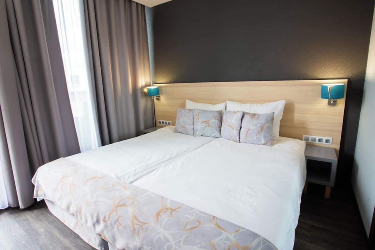 A hotel room with a large bed, two bedside tables, and a headboard with wall-mounted lamps.