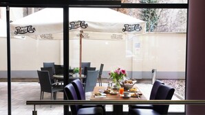 Un espace extérieur aménagé pour les repas, avec des tables, des chaises, des parasols et un vase de fleurs.