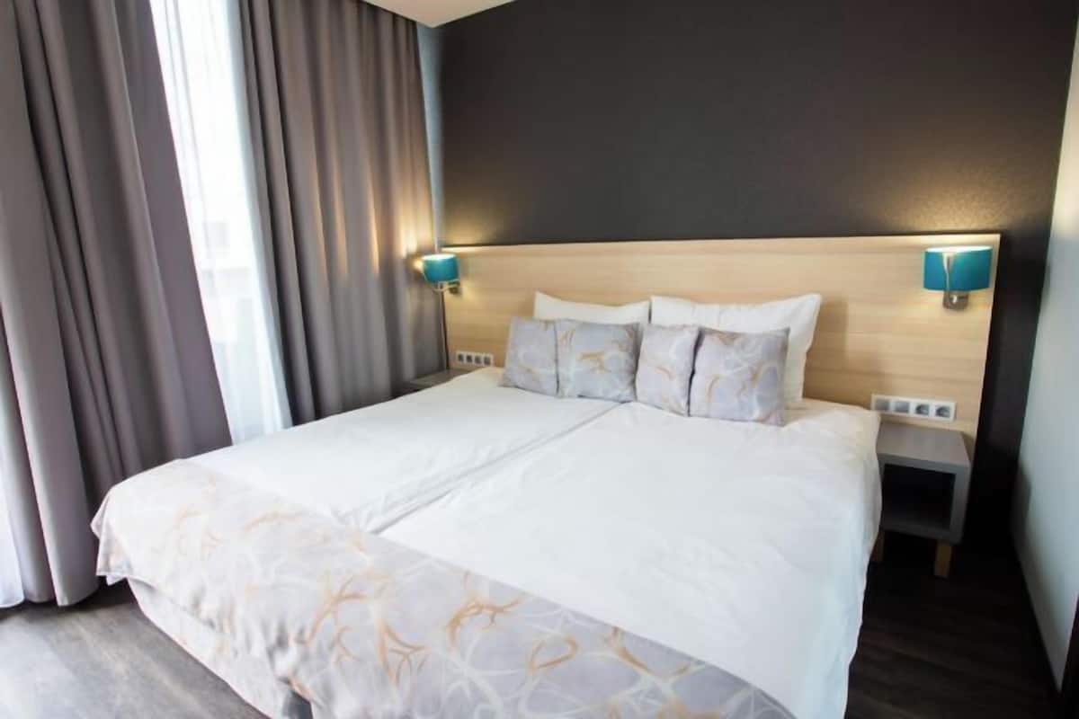 A hotel room with a large bed, two bedside tables, a headboard, and two wall-mounted lamps.