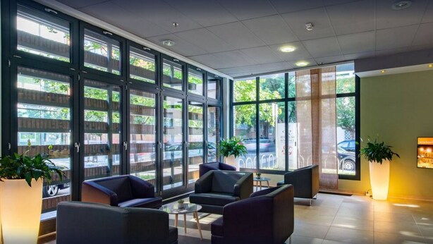 Un hall d’entrée moderne doté de grandes fenêtres, de sièges confortables et d’un téléviseur à écran plat fixé au mur.
