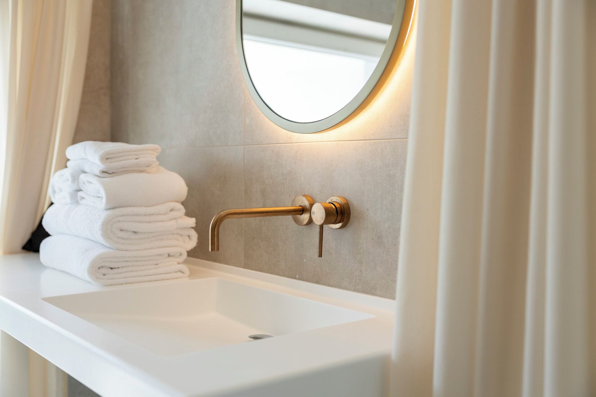 Un bagno con un lavandino bianco, un rubinetto dorato e una pila di asciugamani bianchi.