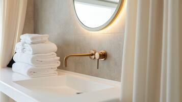 Un bagno con un lavandino bianco, un rubinetto dorato e una pila di asciugamani bianchi.