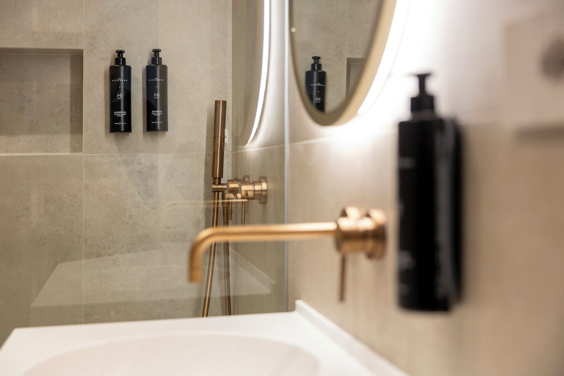Une salle de bain moderne avec une douche à parois de verre, un robinet doré et des articles de toilette noirs fixés au mur.