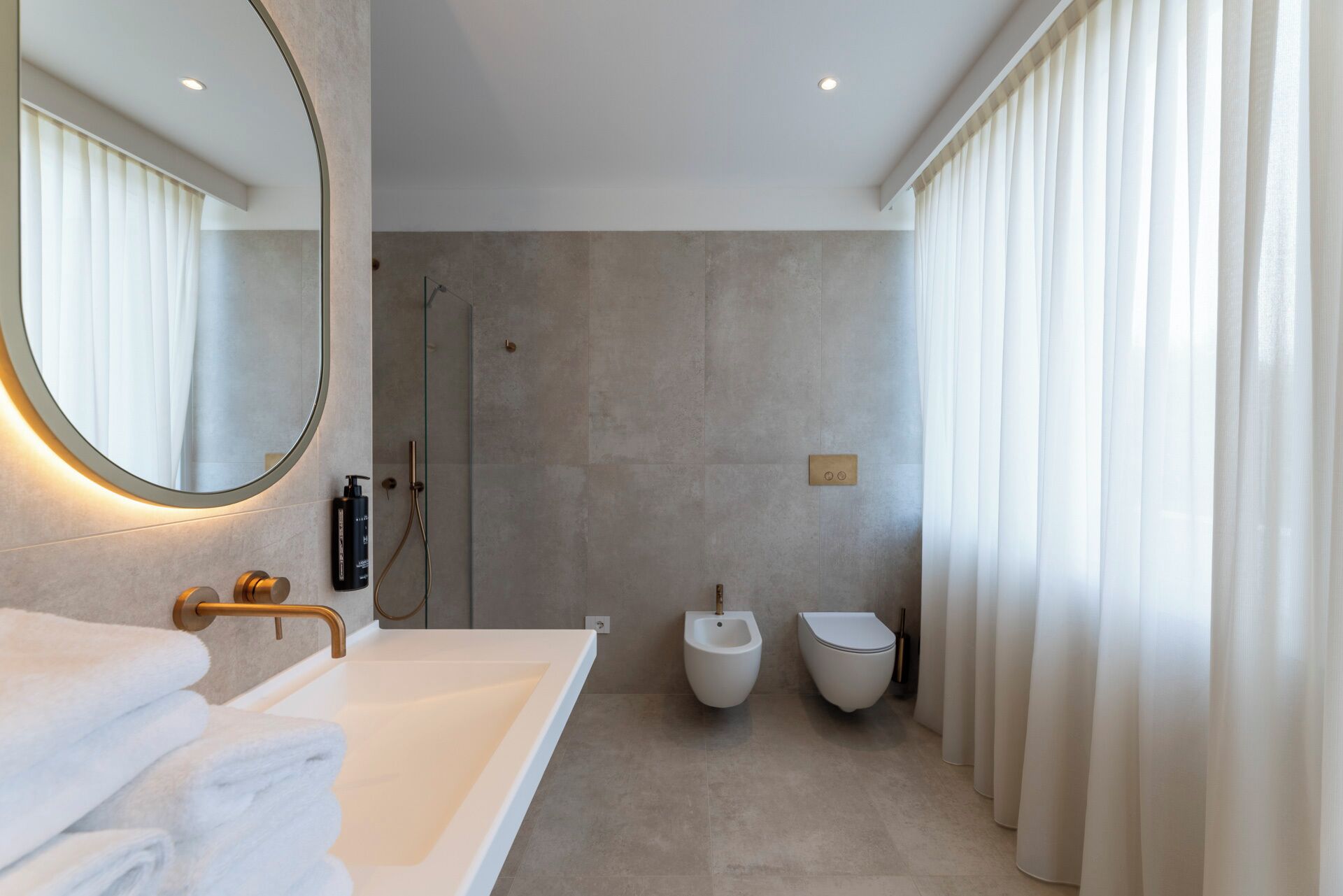 A modern bathroom with a large mirror, a bathtub, a shower, and two toilets.