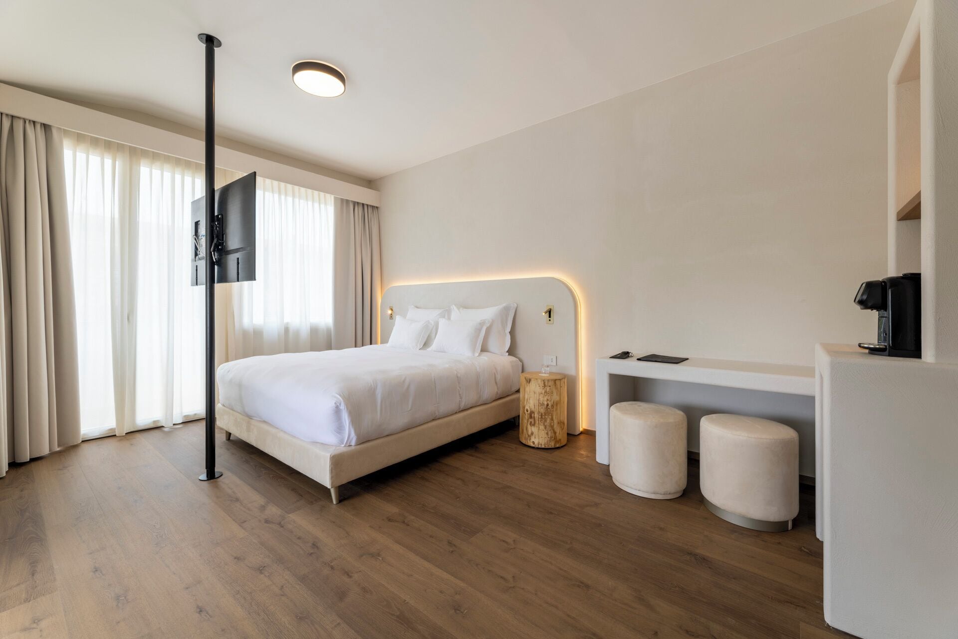 Una habitació d'hotel moderna amb un llit gran, una taula de nit, una màquina de cafè i un televisor muntat a la paret.
