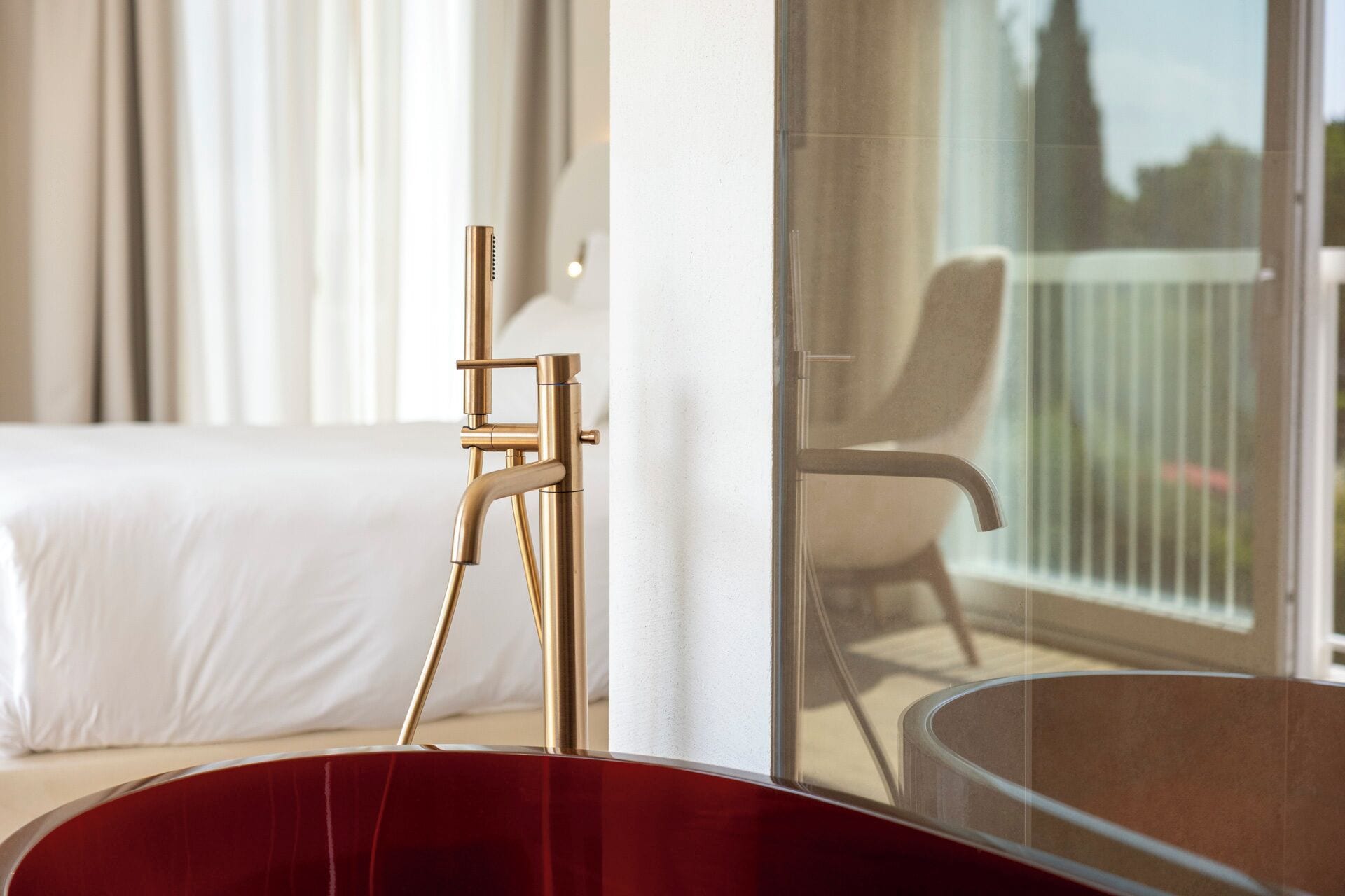 Habitación de hotel moderna con una cama grande, una silla roja y un ventanal de vidrio que da a un balcón.