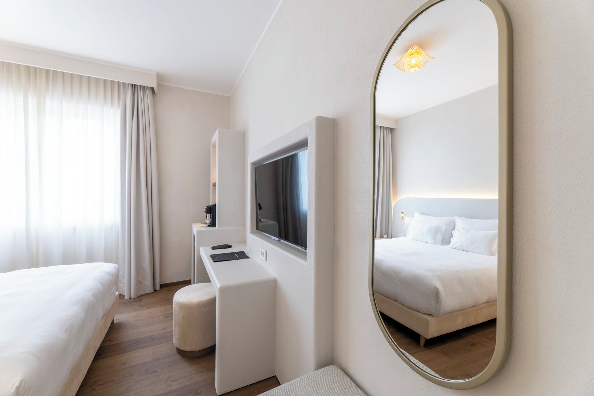 A hotel room with two beds, a desk, a TV, and a large mirror.