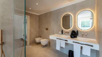 Une salle de bain moderne avec deux lavabos, un bidet et un grand miroir doté d’un éclairage intégré.